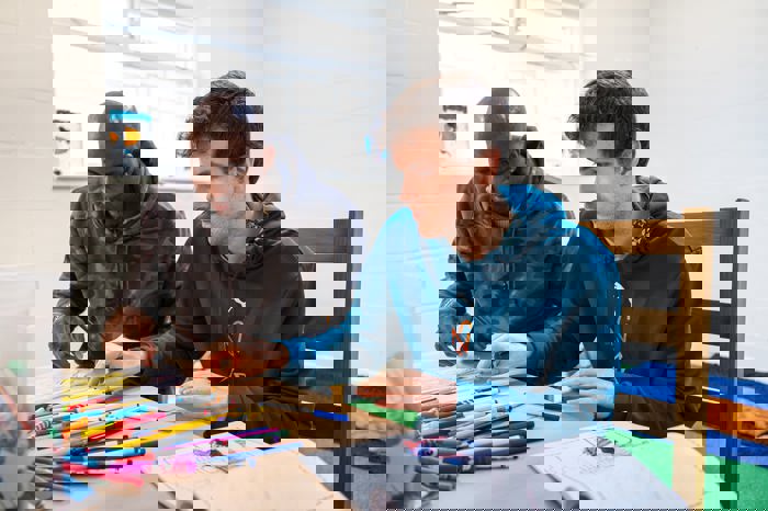 Two men sitting at a table indoors, concentrating as they colour and draw together with pens and colouring books..