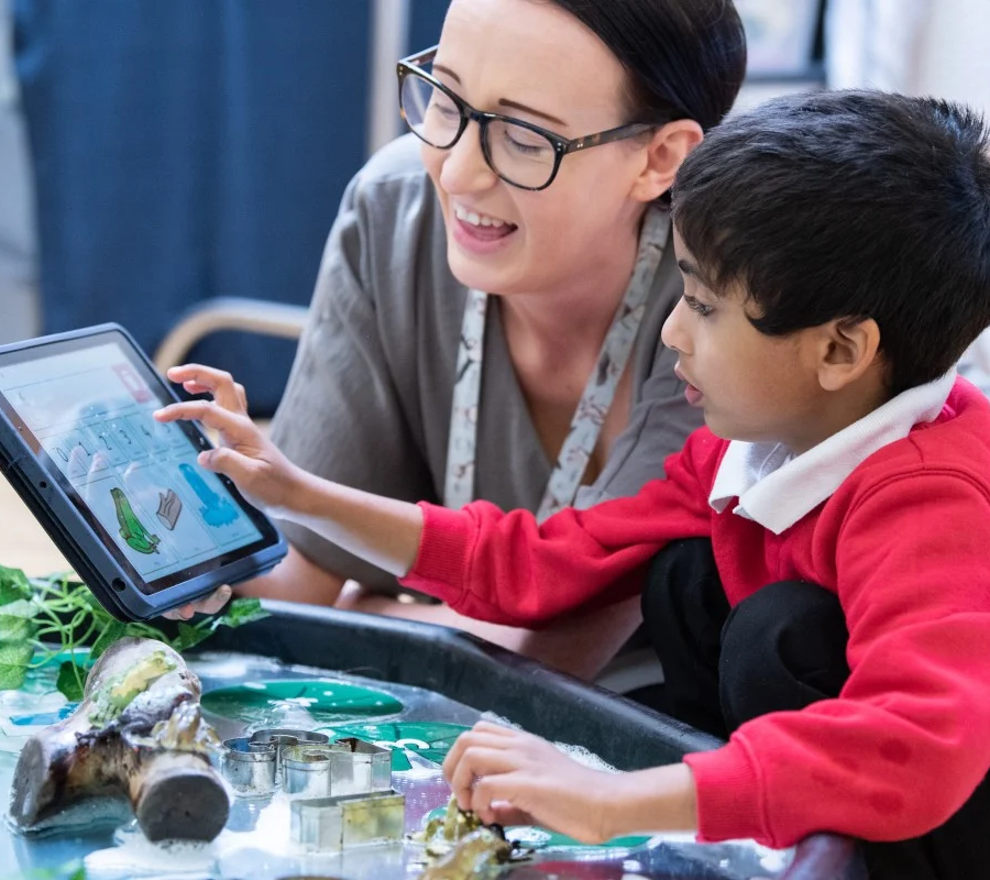 Adult and child using a tablet together during a sensory play activity, with water and natural objects on the table.