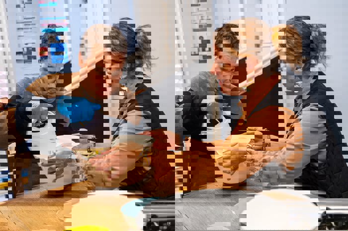 Woman holding a bowl while a man wearing blue gloves mixes the contents with an electric hand whisk